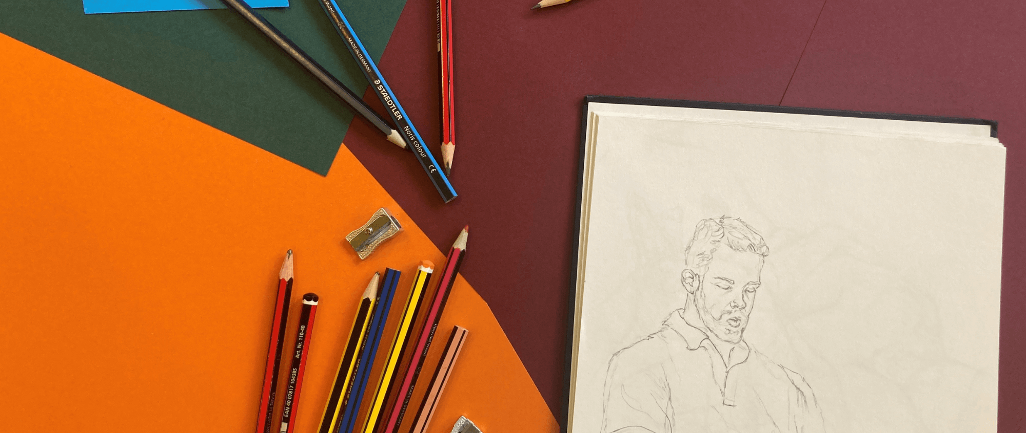 Drawing on a pad with various pencils on a purple, dark green and orange background