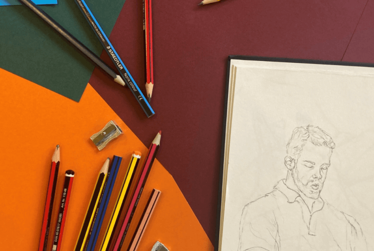 Drawing on a pad with various pencils on a purple, dark green and orange background