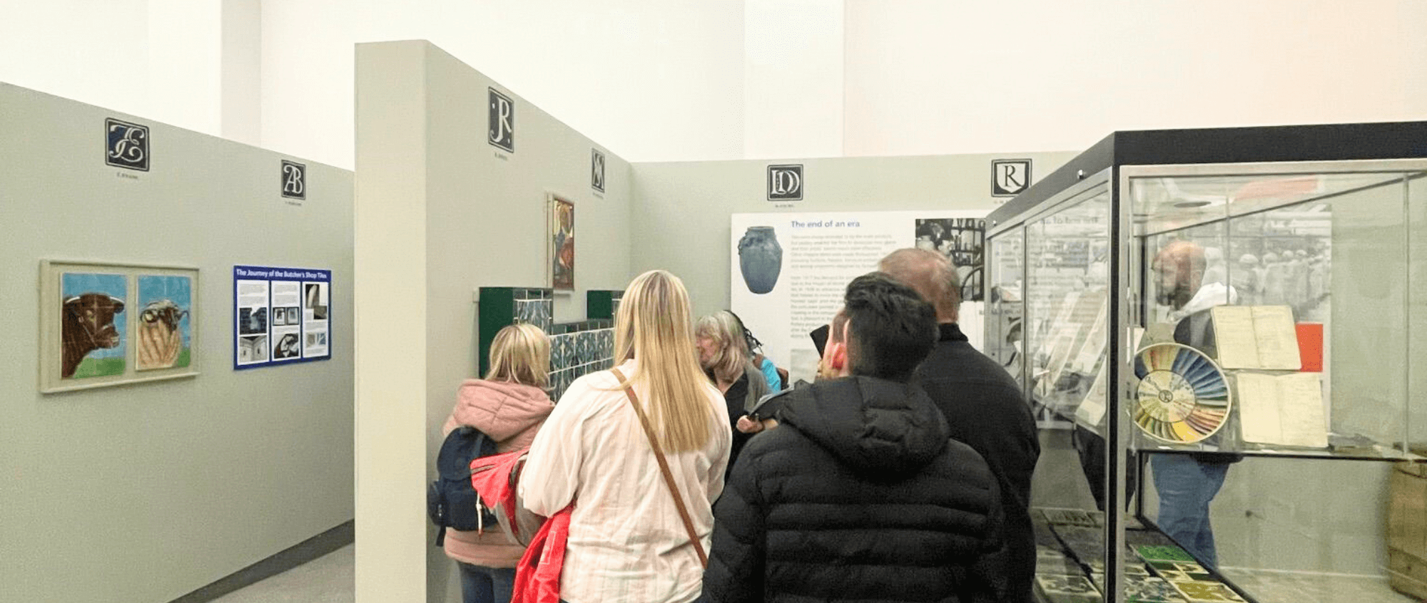 Sight Loss Council – A group of people are gathered in a narrow section of a museum exhibition space, they are all facing the same way.