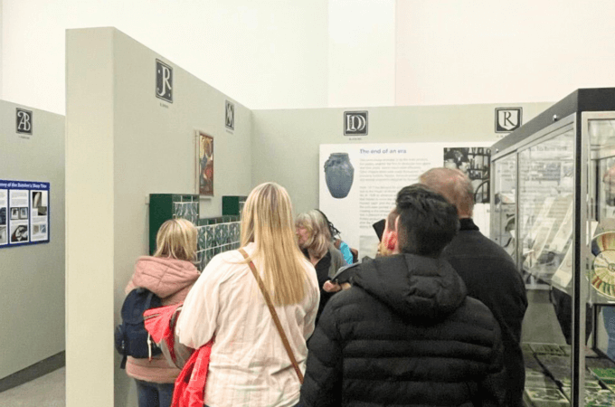 Sight Loss Council – A group of people are gathered in a narrow section of a museum exhibition space, they are all facing the same way.