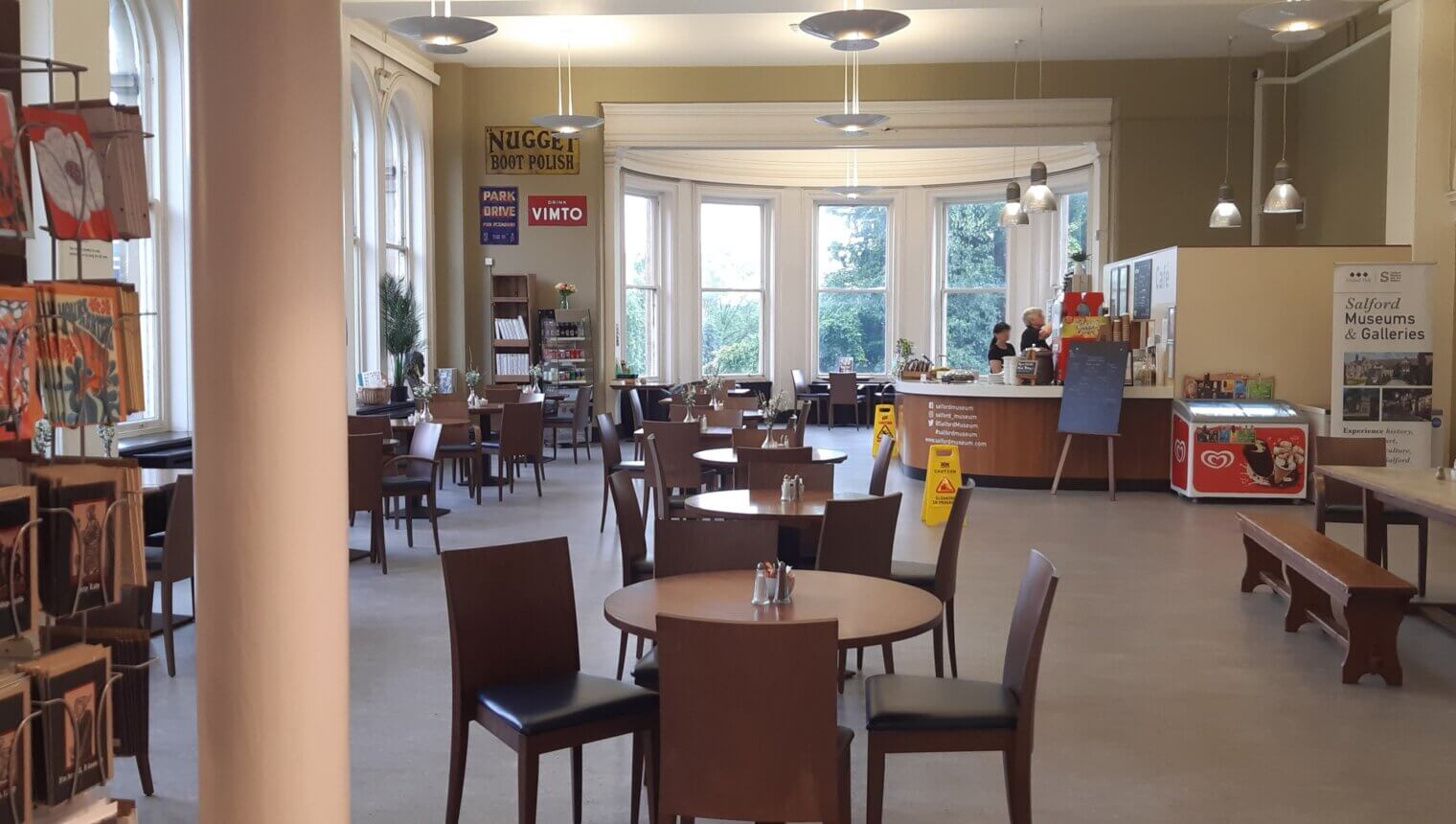 A room with a curved bay window and white columns. There are wooden cafe tables and chairs.