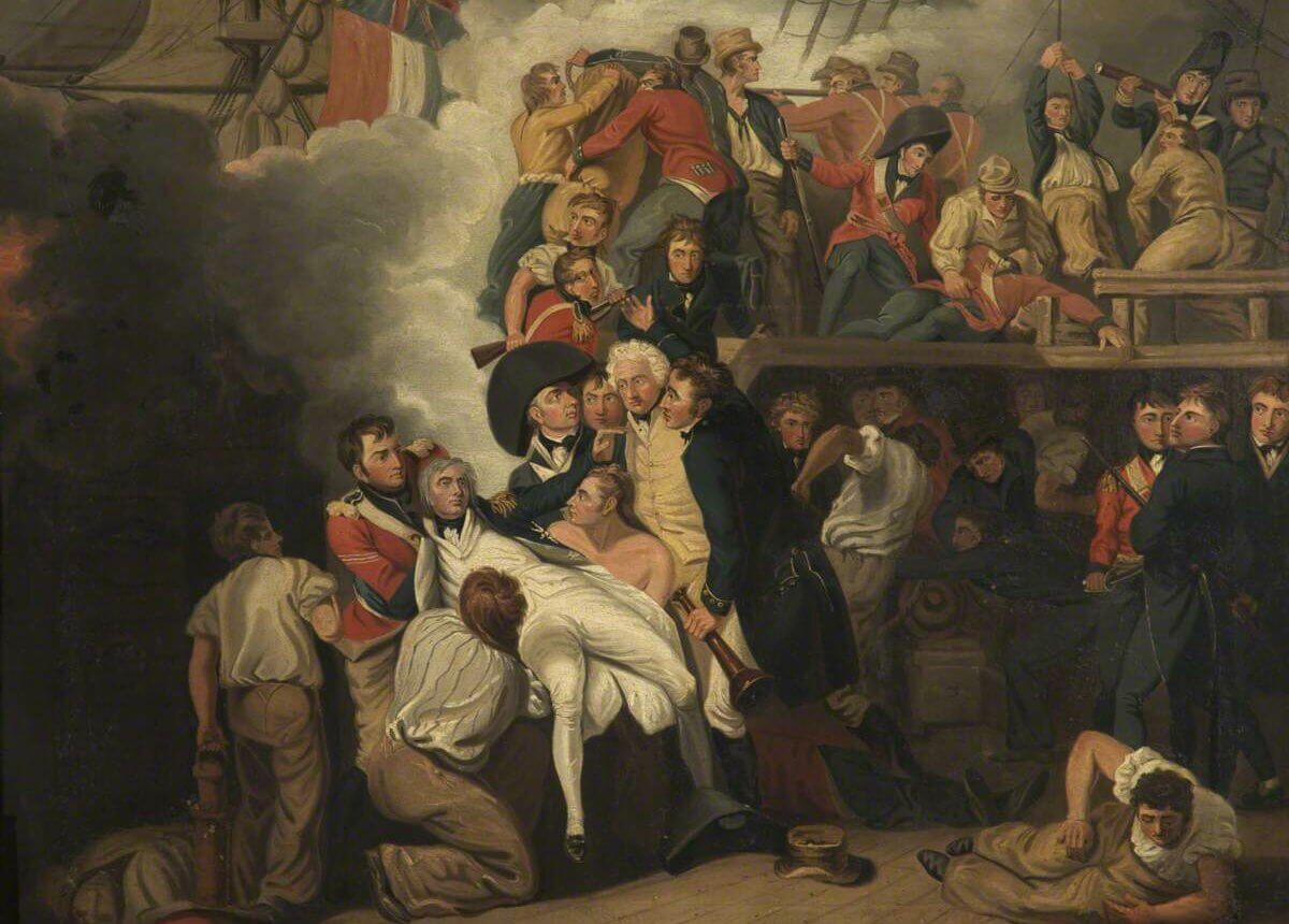 A crowd of men onboard a large ship. They cradle the dead body of Nelson who has been shot. Smoke pours over the side of the ship.