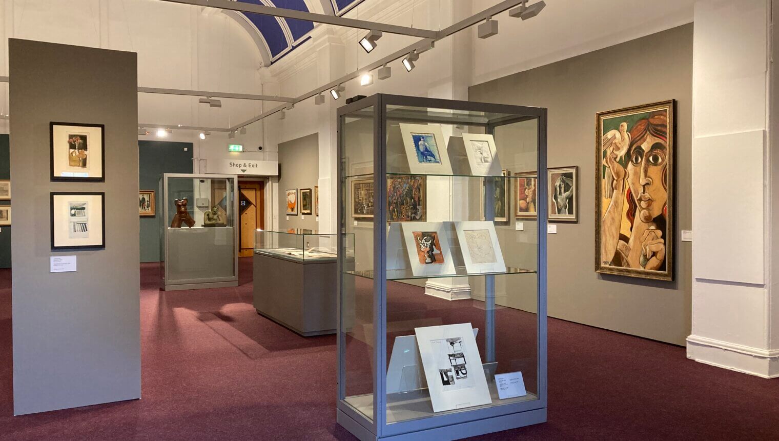 Grey walls with framed paintings hanging on them. Glass cases containing paper prints.