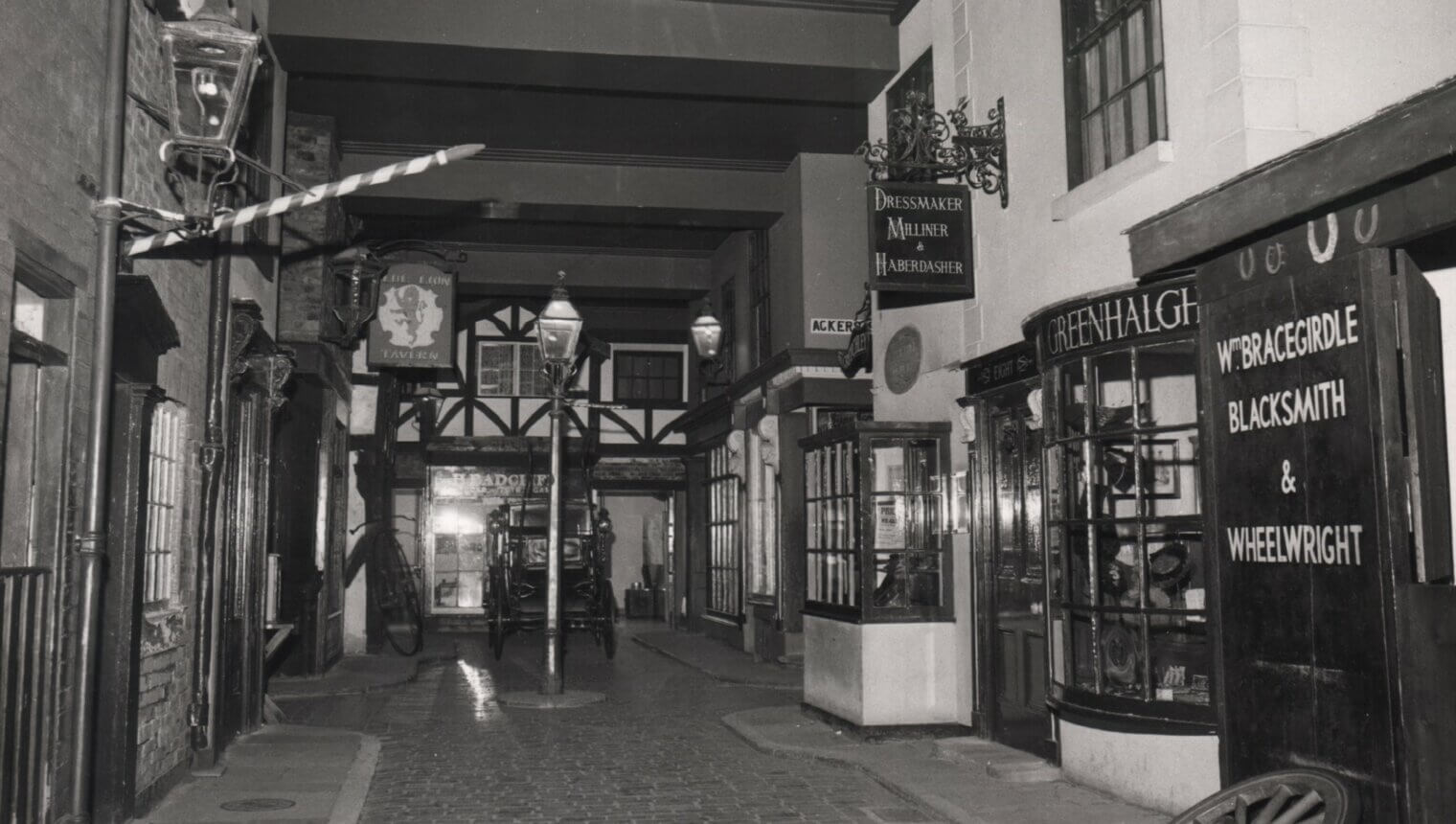 A black and white photo of a fake street with old fashioned shop fronts and cobbled floors.