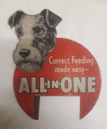 An advert for All-in-One dog food. It has white writing over a red circle and the head of a dog poking over the top.