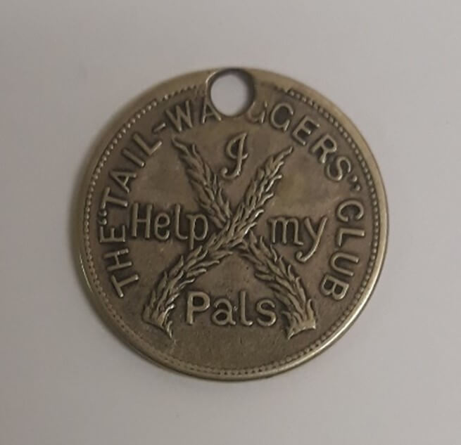 A coin shaped medal for the Tail-Waggers Club. It has two tails forming a cross in the middle and the text reads 'I help my pals'.