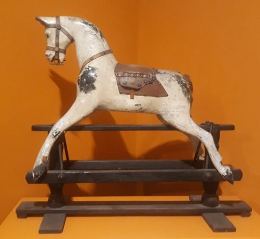 A white rocking horse with a brown saddle.
