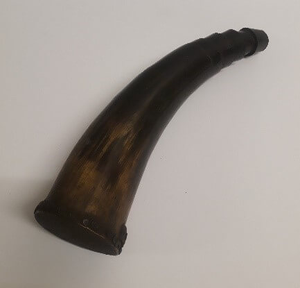 A dark brown and black animal horn with ridges carved at the point forming the mouthpieces of an instrument.