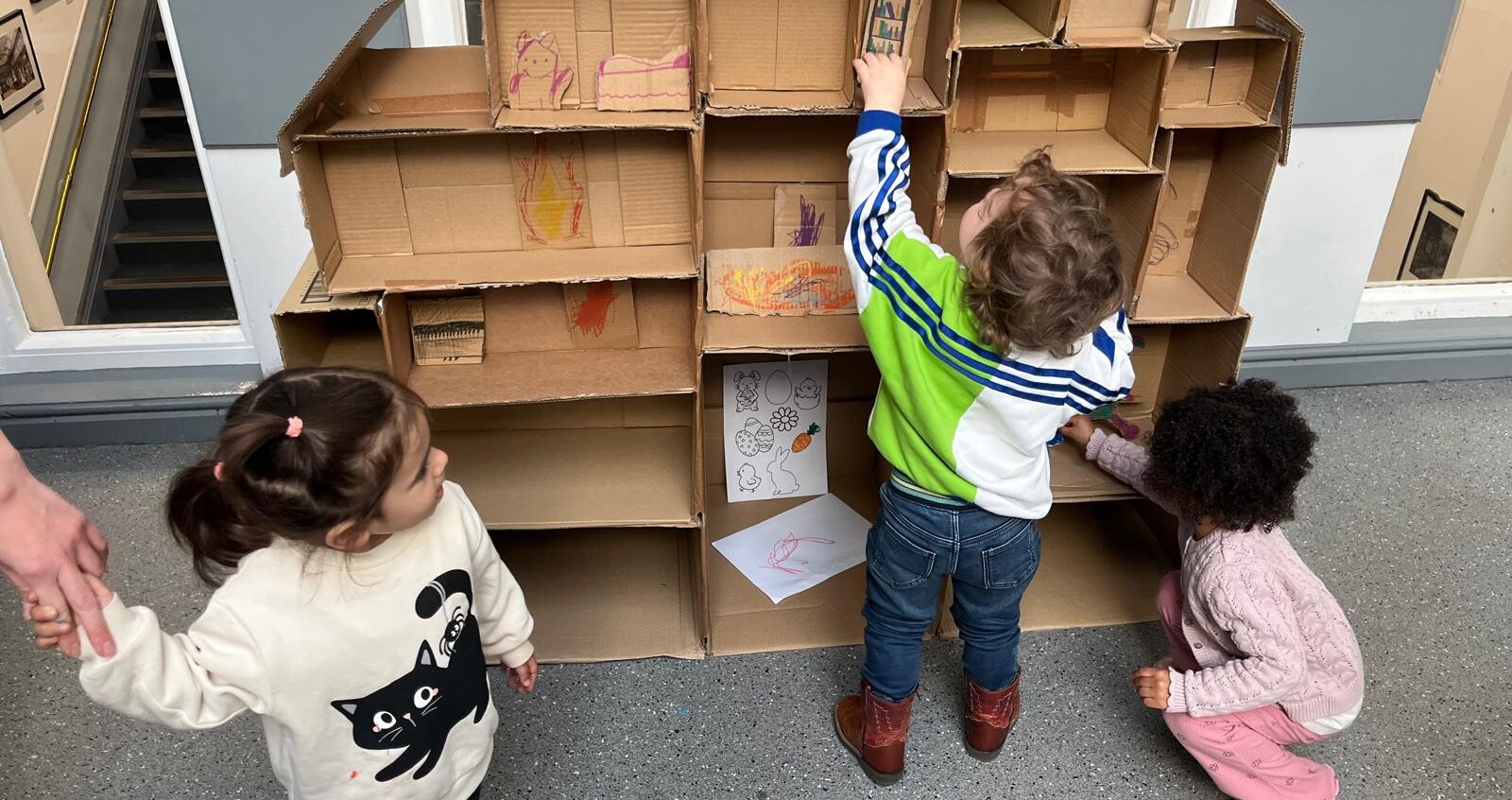 Three children are helping decorate our cardboard dolls house